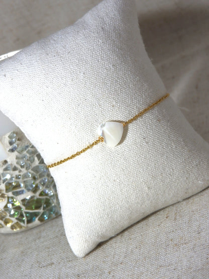 Bracelet chaîne fine en acier inoxydable doré posé sur un mini-coussin beige en coton. Bijou orné d'une perle coeur en nacre blanche.