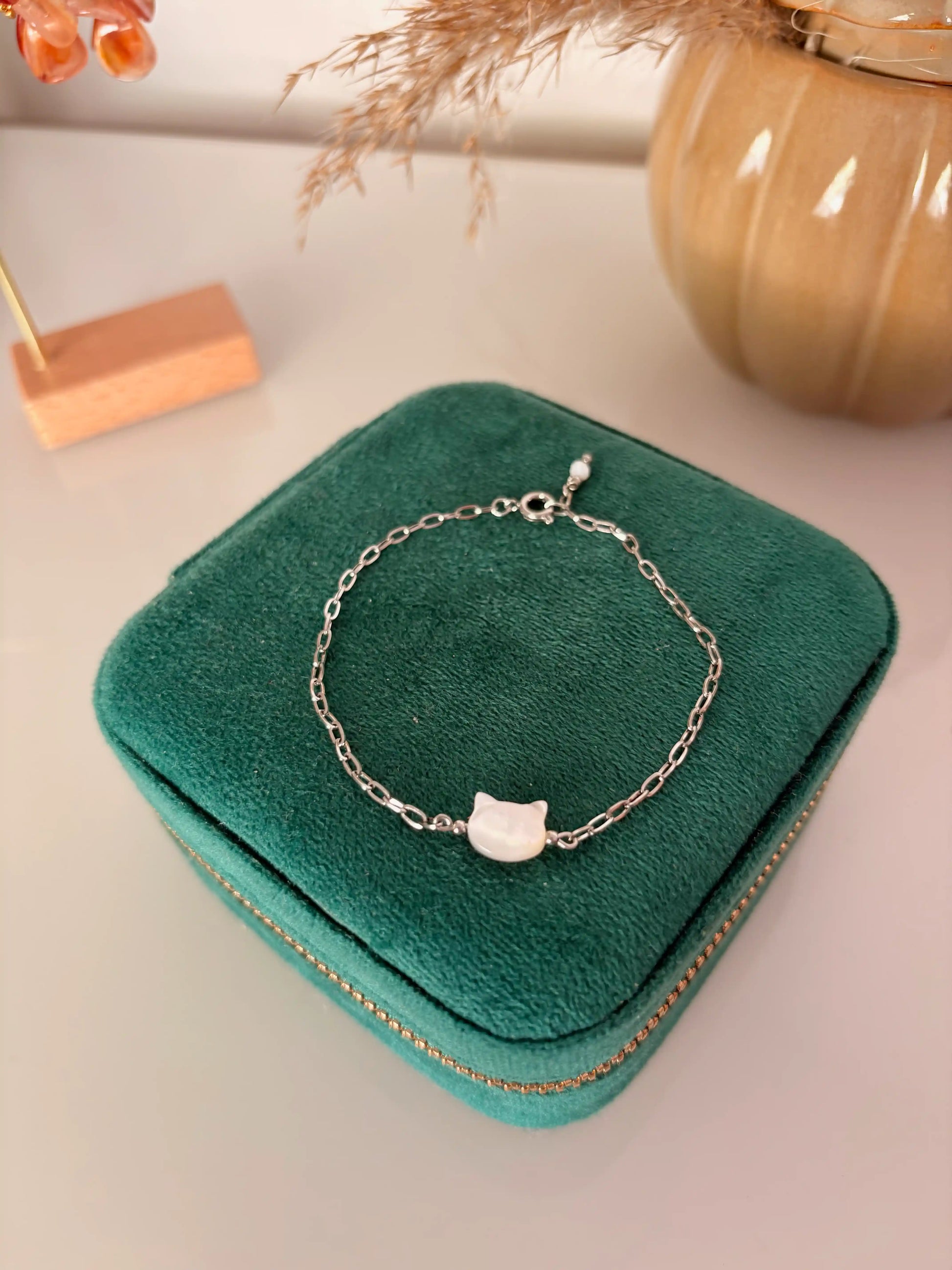 bracelet chaine à maille rectangle en acier inoxydable argenté disposé sur une boite à bijoux. Bijou orné d'une perle chat en nacre blanche.