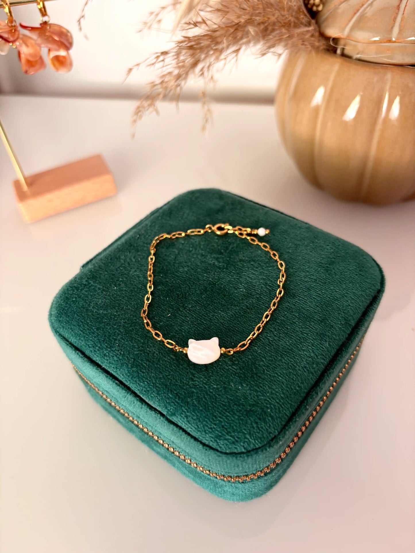 bracelet chaine à maille rectangle en acier inoxydable doré disposé sur une boite à bijoux. Bijou orné d'une perle chat en nacre blanche.