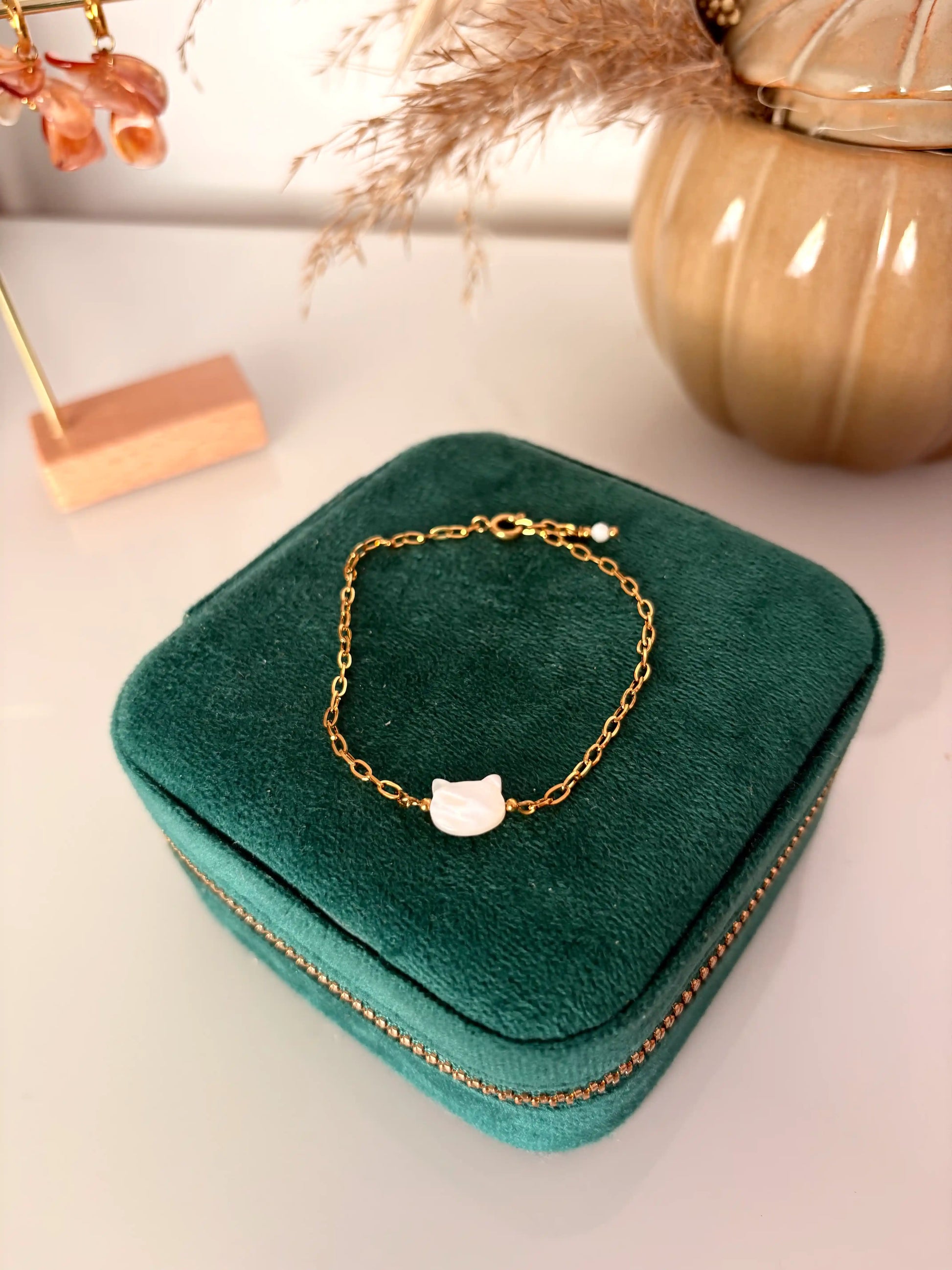bracelet chaine à maille rectangle en acier inoxydable doré disposé sur une boite à bijoux. Bijou orné d'une perle chat en nacre blanche.