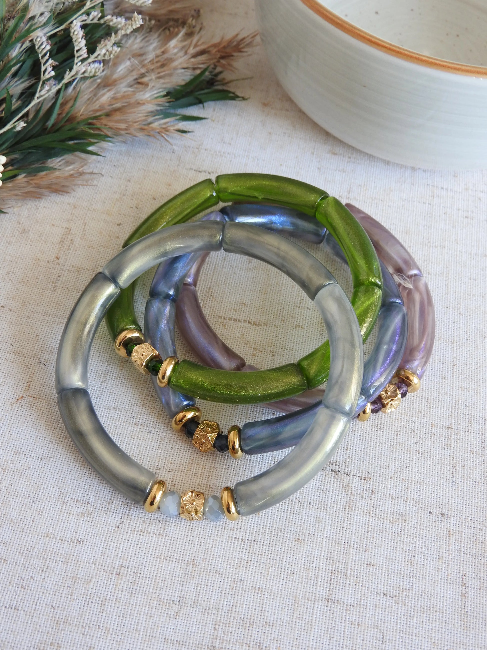 quatre bracelets joncs élastiqués en perles tube colorées vert, gris, bleu et parme irisés. Bijoux ornés de perles de verre et perles rondelle et cube au motif fleuri en acier inoxydable doré. Bijoux superposés les uns sur les autres.