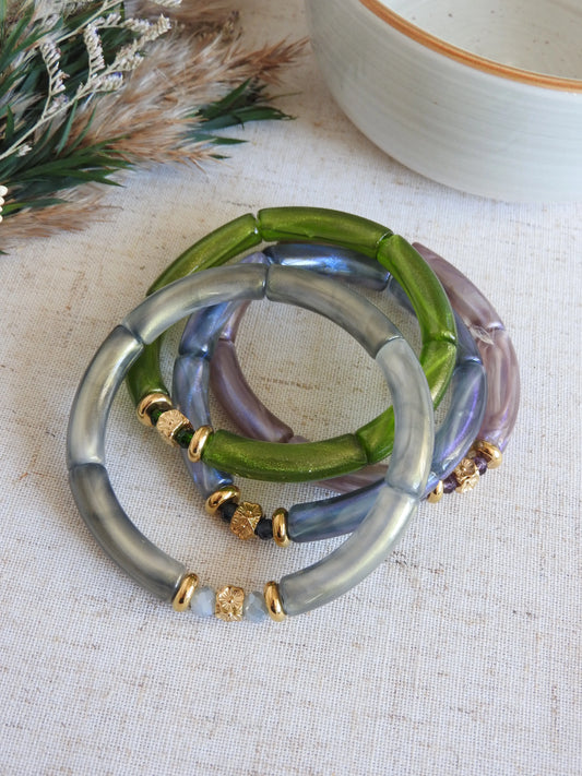 quatre bracelets joncs élastiqués en perles tube colorées vert, gris, bleu et parme irisés. Bijoux ornés de perles de verre et perles rondelle et cube au motif fleuri en acier inoxydable doré. Bijoux superposés les uns sur les autres.