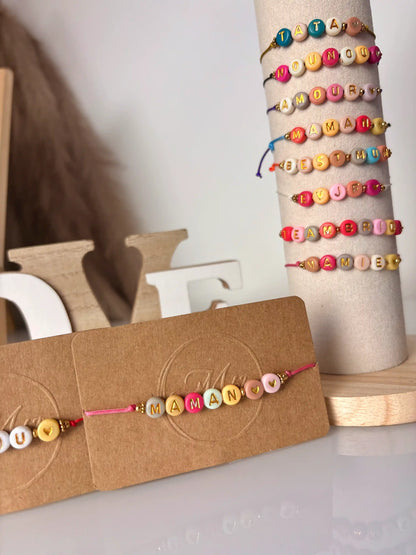 Bracelets à cordon coloré avec un message en perles colorées à personnaliser. Bijoux présentés sur un support tube vertical et un carton kraft.