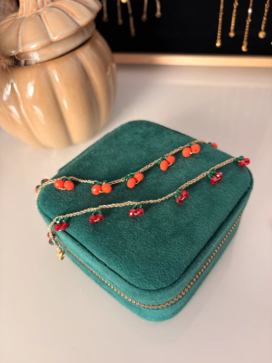 bracelets à fil crochetés doré présentés sur une boite à bijoux vert. Bracelets ornés de perles de verre formant des petites cerises et des petites oranges. 