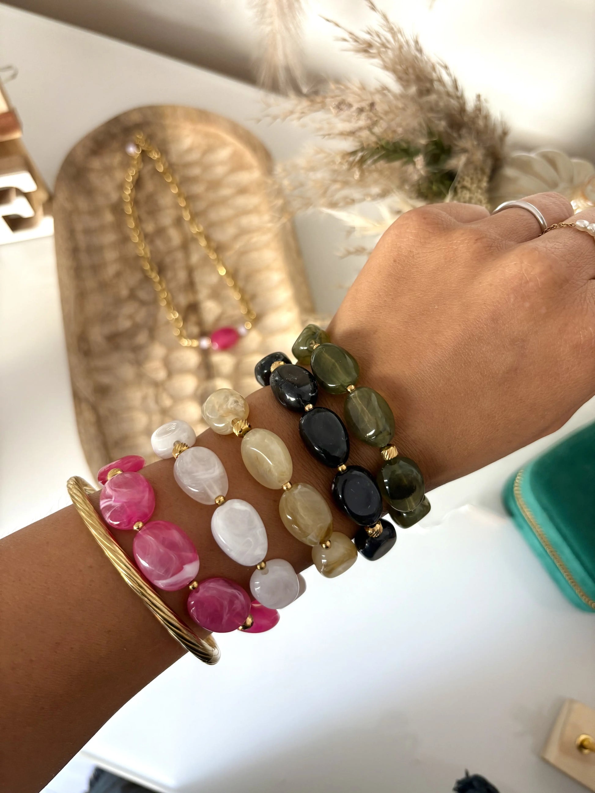 bracelets à grandes perles colorées portées au bras avec un jonc doré. Perles de coloris rose, blanc, kaki, noir et vert olive. 