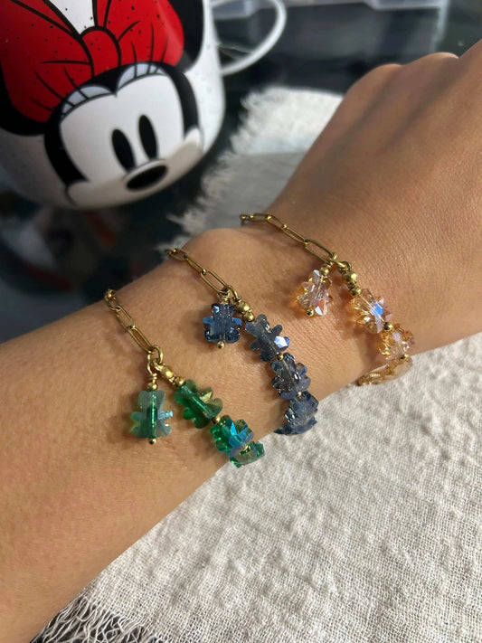 trois bracelets portés au poignet posée sur une table décoré d'une tasse minnie. Bracelets mi-chaîne à maille rectangle en acier inoxydable doré et mi-perles de verre en forme d'ours colorées bleu nuit, beige et vert.