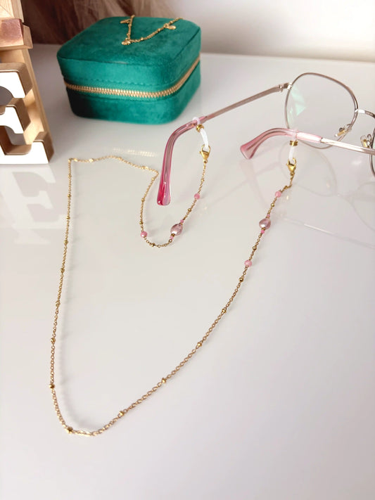Chaîne de lunettes en acier inoxydable doré perlée et ornée de perles d'eau douce rose et en verre rose. Accessoire bijou présenté avec des lunettes aux branches roses. 