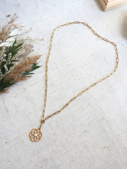 collier chaîne à maille rectangle en acier inoxydable doré posé à plat sur une nappe beige. Bijou orné d'un pendentif fleur filigrane en acier doré, orné d'une pierre de lune.