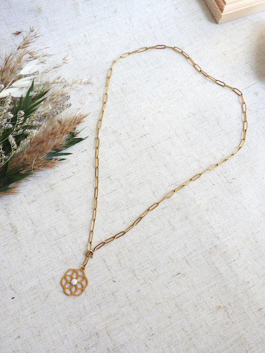 collier chaîne à maille rectangle en acier inoxydable doré posé à plat sur une nappe beige. Bijou orné d'un pendentif fleur filigrane en acier doré, orné d'une pierre de lune.