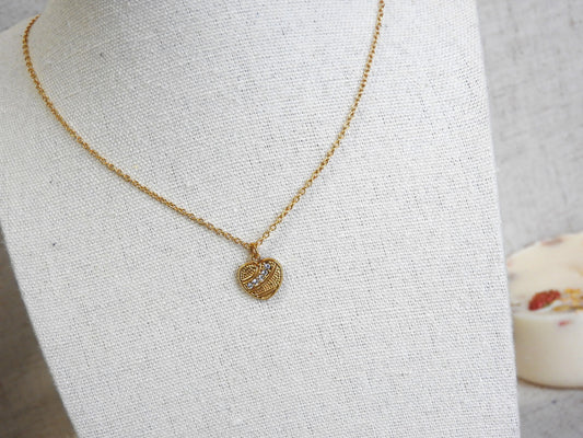 Collier chaîne fine et pendentif cœur texturé orné de pierres en oxydes de zirconium et en acier inoxydable doré. Bijou posé sur un buste en coton beige.