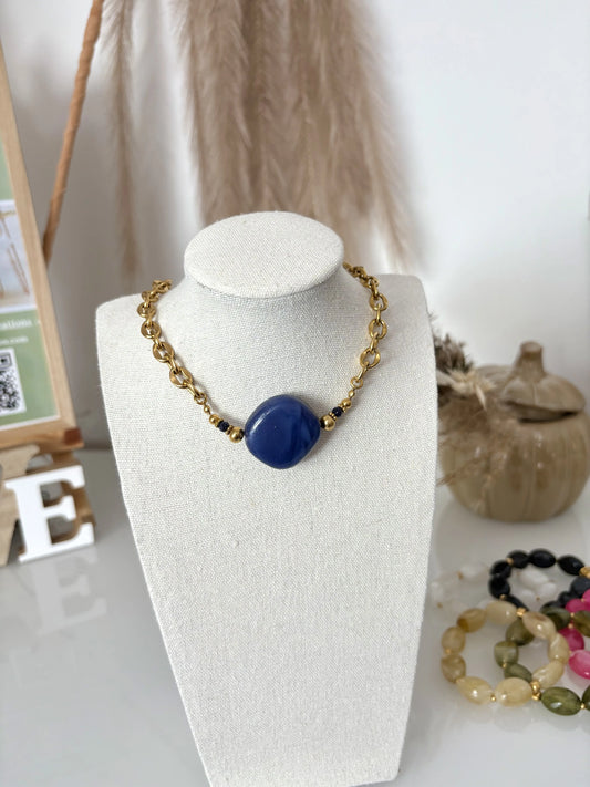 collier choker grosses mailles en acier inoxydable doré et perle losange bleu-gris scintillant. Bijou présenté sur un buste en coton