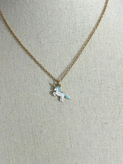 Collier pour enfant à chaîne fine posé à plat sur une nappe beige. Bijou orné d'un pendentif licorne blanche en résine époxy et acier inoxydable doré. 