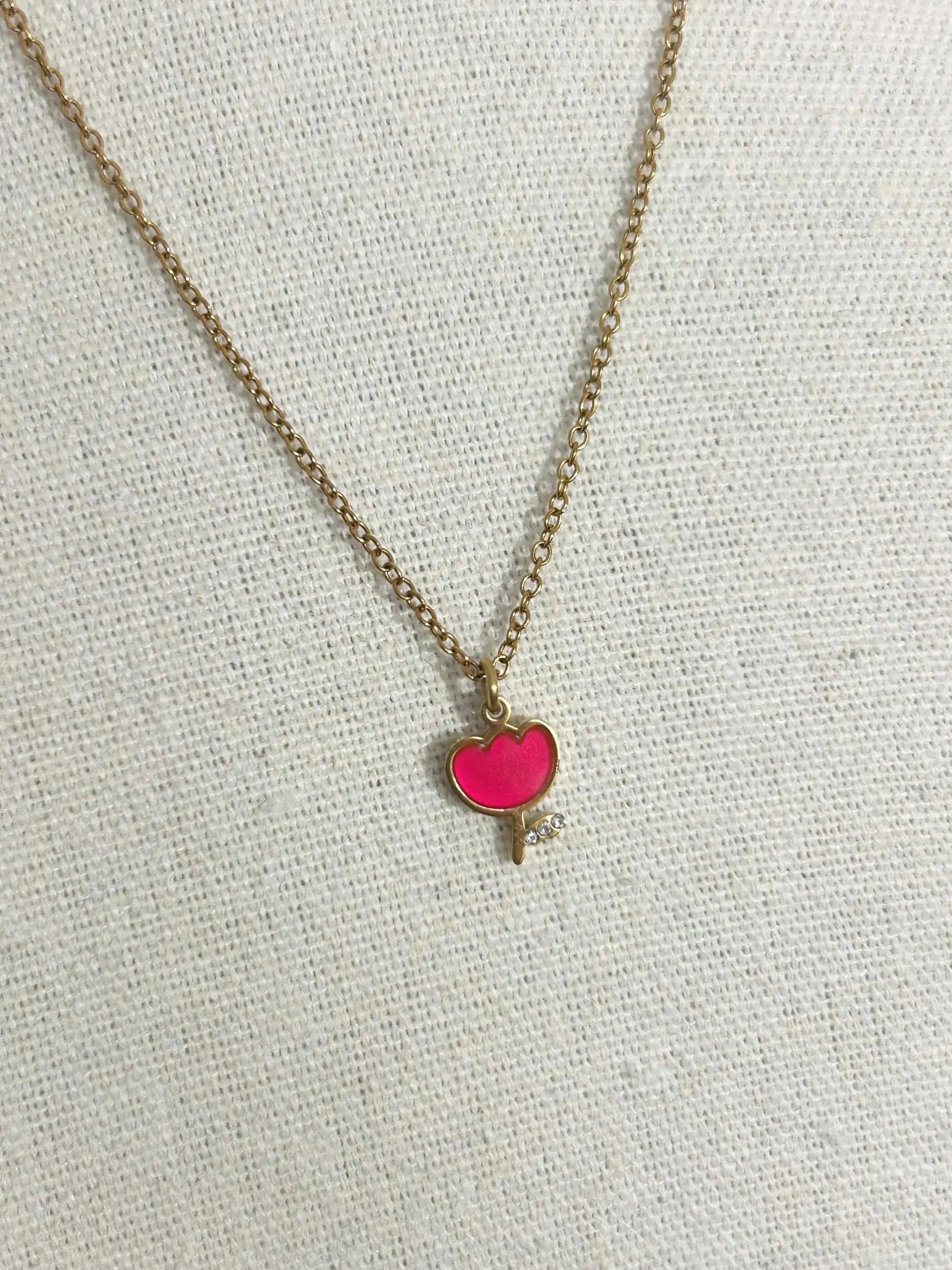 Collier pour enfant à chaîne fine posé à plat sur une nappe beige. Bijou orné d'un pendentif tulipe rouge en résine époxy et acier inoxydable doré. 