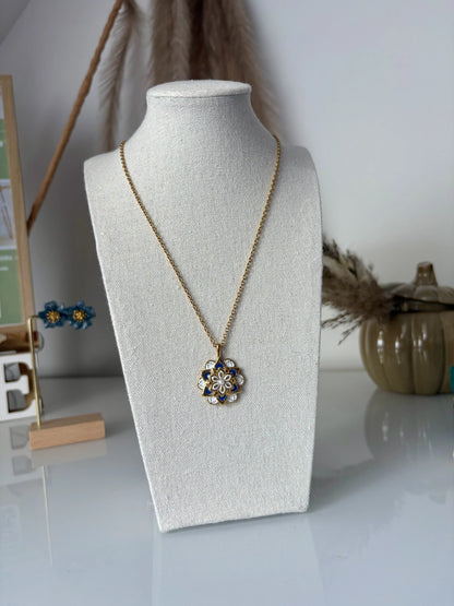 Collier sautoir en acier inoxydable doré présenté sur un buste présentoir. Bijou orné d'un pendentif mandala bleu et blanc en résine époxy et en acier inoxydable doré.