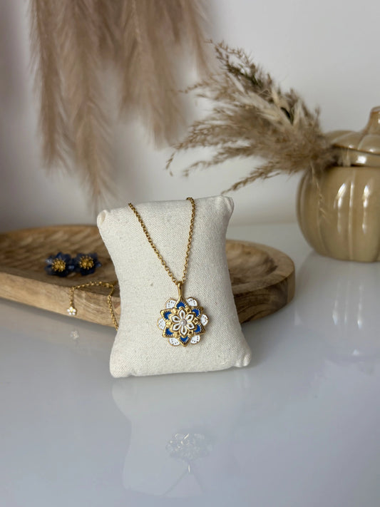 collier sautoir mandala bleu et blanc en acier inoxydable doré et résine époxy. Bijou présenté sur un mini-coussin beige, disposé sur une table en verre trempée et décorée d'un bol citrouille kaki et des brindilles, ainsi qu'un plateau en bambou où sont déposées des boucles d'oreilles bleu.