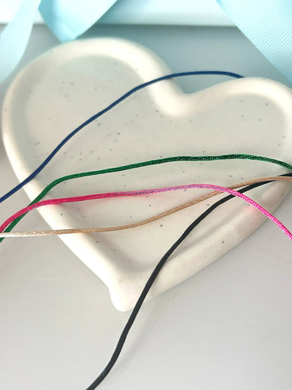 cordons en nylon colorés bleu roi, vert électrique, rose fuchsia, champagne et noir posés sur une coupelle coeur en céramique blanche.