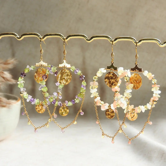 Deux paires de boucles d'oreilles crochets suspendues à une barre métallique dorée. Créoles en suspension décorées de perles de verre faisant le tour de couleurs sable, blanc et jaune pour la première paire et violet, péridot pour la deuxième. Chaînette pendante avec une décoration de sequin martelé.