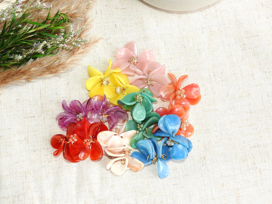 Suspensions de pétales en acrylique formant des bouquets floraux pour boucles d'oreilles créoles en acier inoxydable doré de la marque de bijoux M'Joy Creation. Suspensions florales disposées à plat sur une nappe beige en coton.