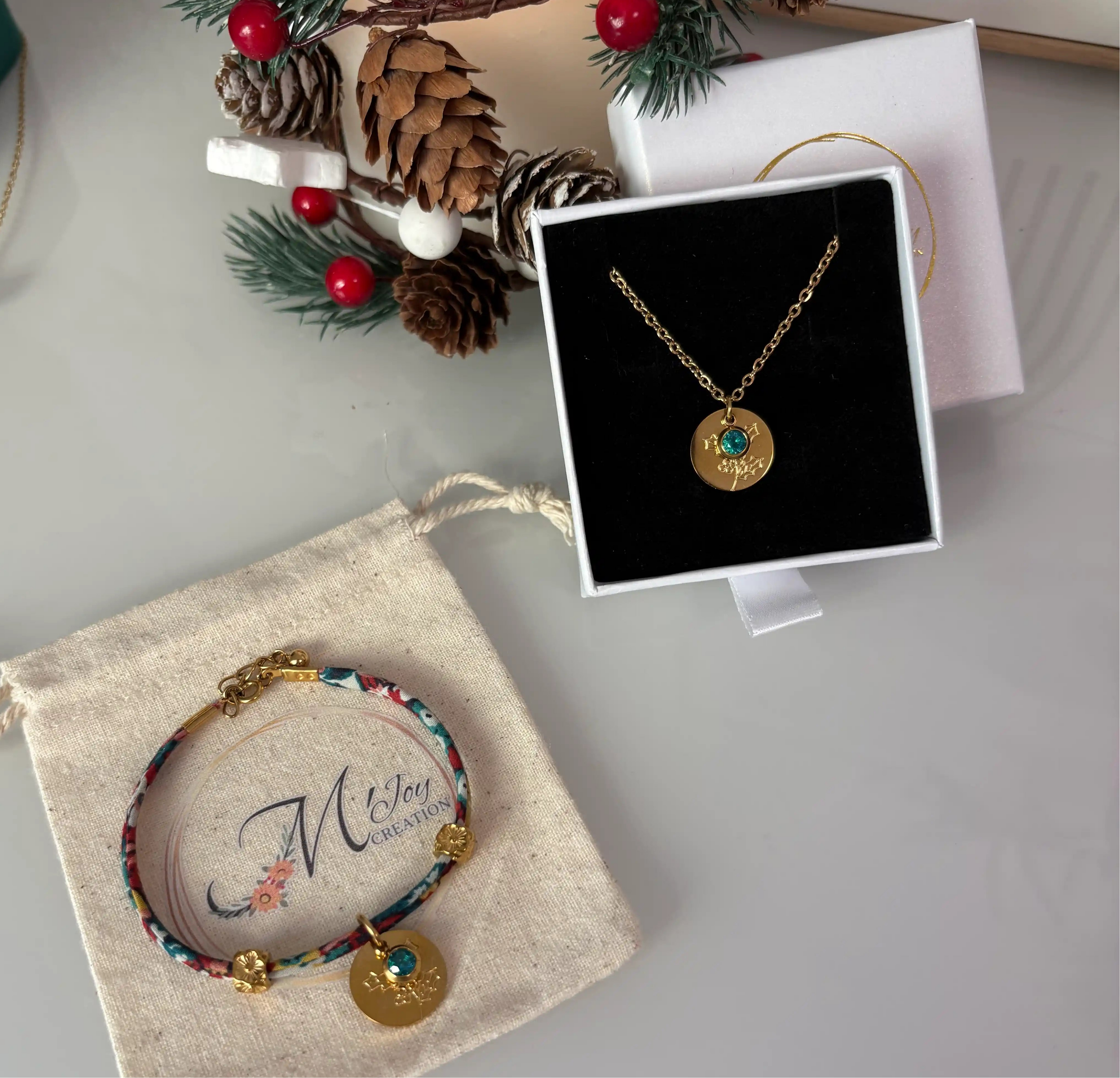 Parure présentée dans un écrin et un pochon à bijou. Collier chaîne en acier inoxydable doré avec une médaille fleur de naissance et pierre de naissance bleu zircon symbole du mois de décembre. Bracelet cordon liberty fleuri avec les mêmes breloques.